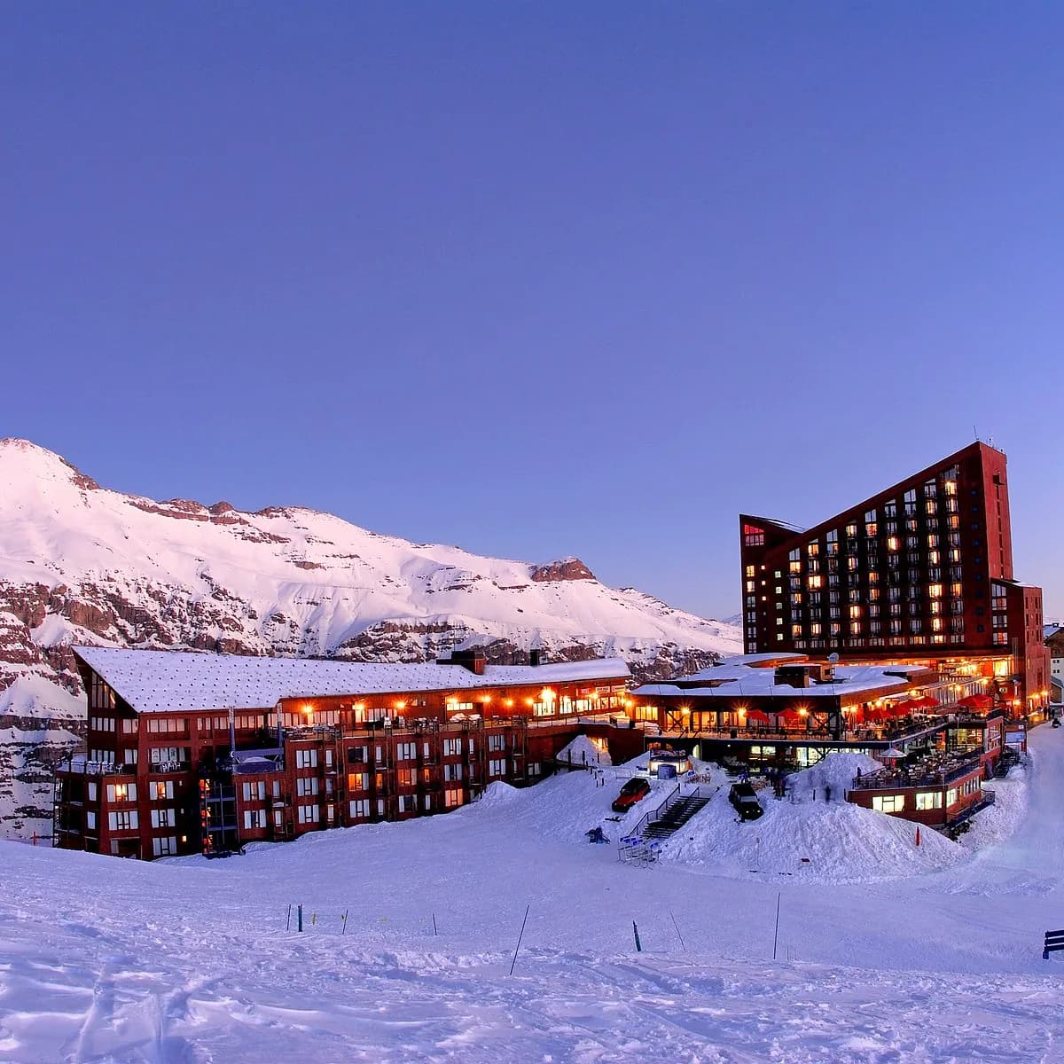 Hotel y edificios de Valle Nevado iluminados al atardecer, con montañas cubiertas de nieve